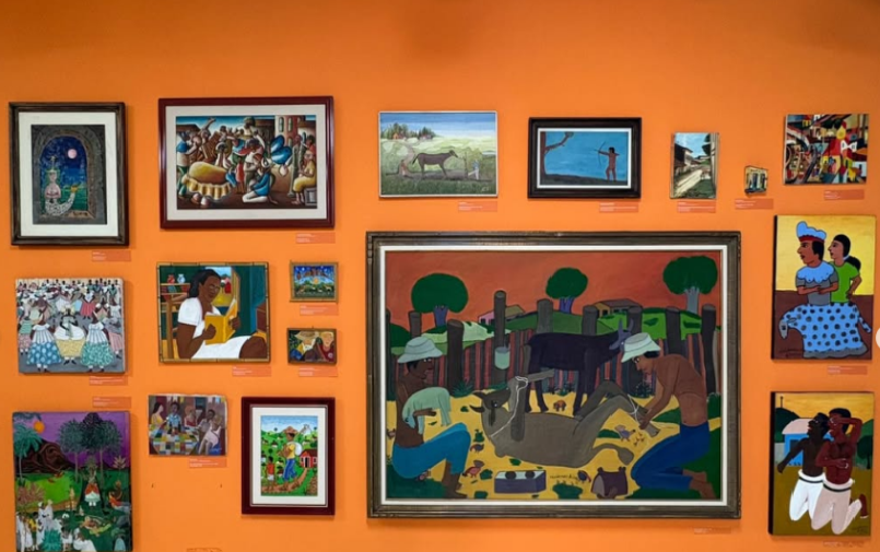 Parede laranja com quadros de artistas que estão exposto na sala permanente do museu, destaque para as cores vibrantes das obras.