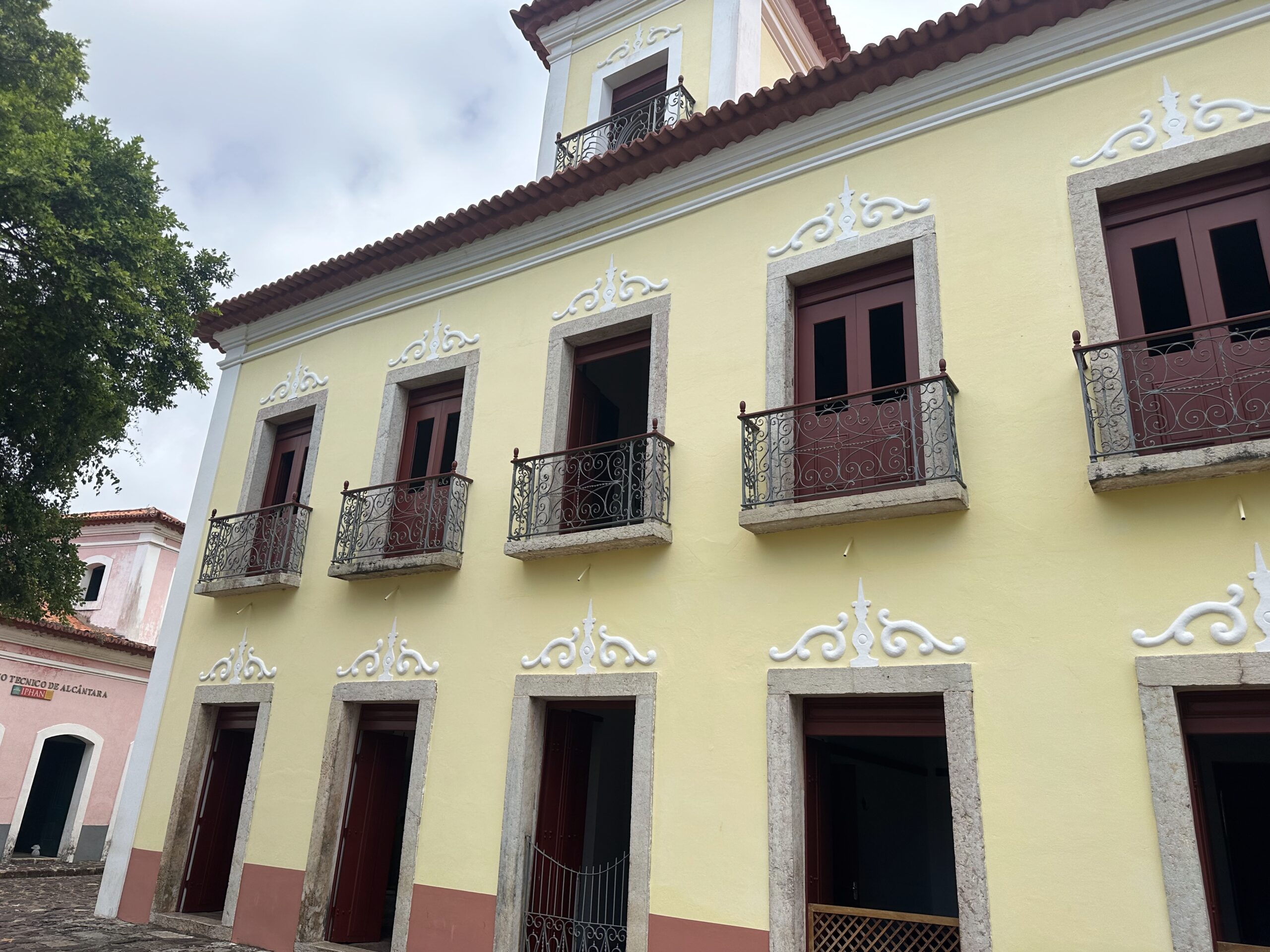 Fotografia da fachada do museu, com destaque para os dois andares que possuem pintura das paredes em amarelo, com portas e janelas em tom escuro. Acima desses, a edificação apresenta um terceiro volume que se sobressai na cobertura, tipo mansarda.