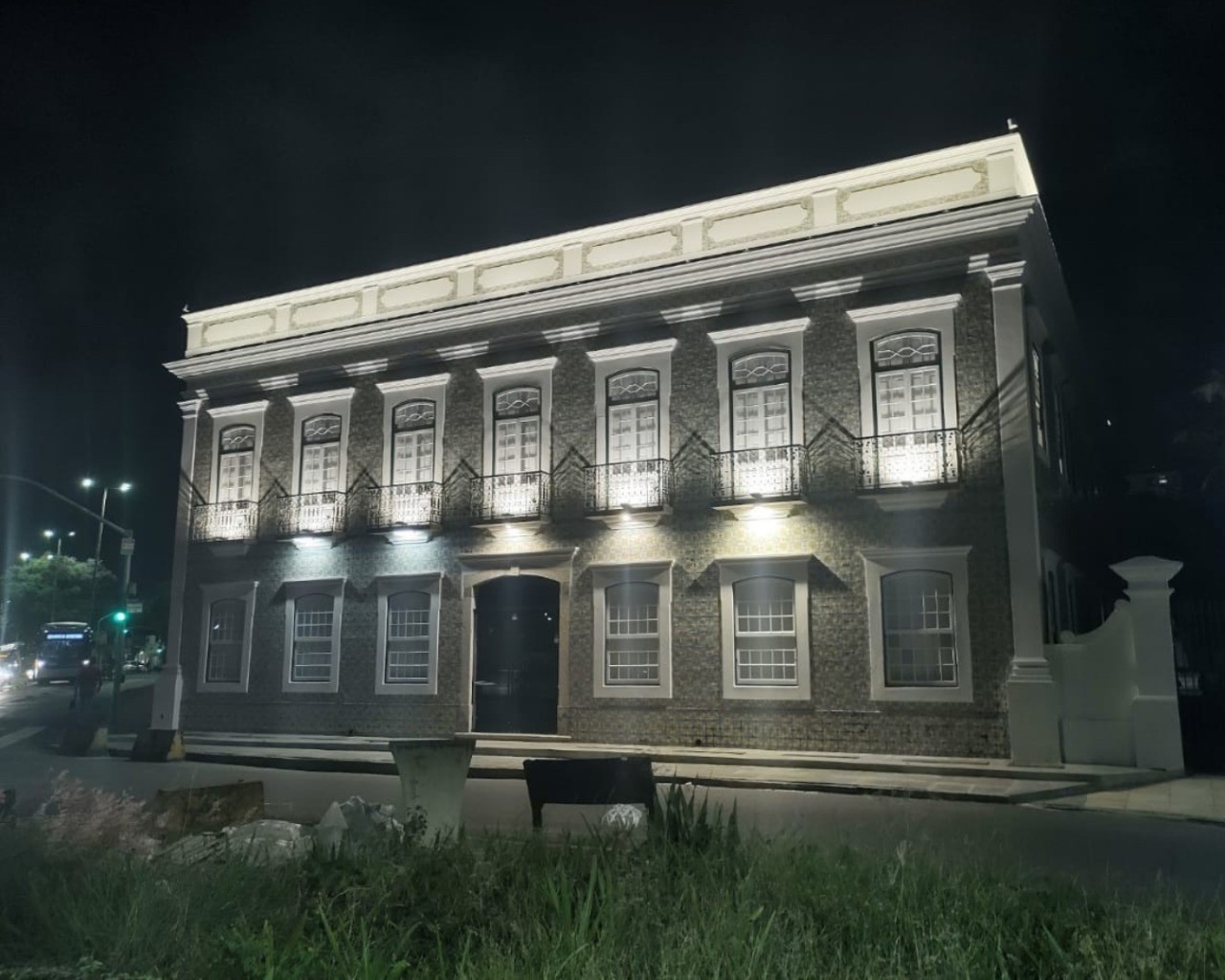 Fachada do museu durante a noite, ressaltando os detalhes das paredes e elementos decorativos, como cornijas e esquadrias. Apresenta uma simetria demonstrada pelas luzes direcionadas, que destacam o ritmo e a dinâmica da composição arquitetônica.