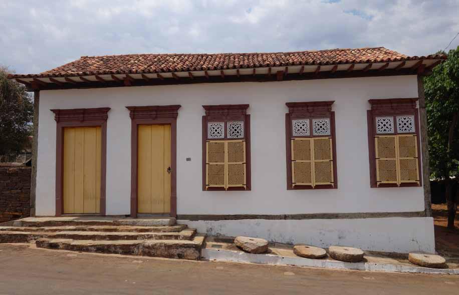 Fotografia da fachada do Museu Casa da Princesa, construção com paredes brancas e cobertura em telhas cerâmicas. A fachada possui duas portas pintadas de amarelo e três janelas com treliças pintadas em amarelo e branco. As portas e janelas são emolduradas por perfis de madeira em tom avermelhado na parte superior. Em frente à casa, há uma pequena escada de pedra que leva à entrada principal.