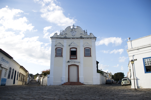 Fotografia da fachada frontal do Museu, construção em estilo colonial com destaque para as esquadrias e a entrada principal demarcada por frontão ornamentado na platibanda do corpo central. No entorno do edifício, há prédios históricos. A imagem é captada durante o dia, com céu azul e nuvens.